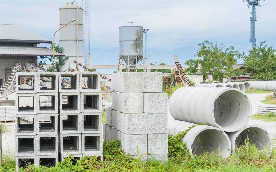 Concrete blocks and cylindrical structures in a precast factory yard with industrial equipment in the background.